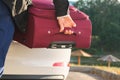 The trunk of a white car, the hands of a man, load a red suitcase, close-up