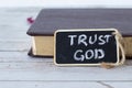 Trust God, a handwritten text on a small blackboard with chalk and a closed Holy Bible Book with golden pages in the background