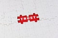 TRUST text on white jigsaw puzzle with missing piece on red.