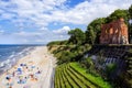 Single wall of ruined church on the edge of cliff, people on the sandy beach below