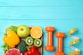 Fruits, vegetables, measuring tape and dumbbells on light blue wooden background, flat lay with space for text. Visiting