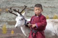 Tsaatan boy, dressed in a traditional deel with a reindeer in a