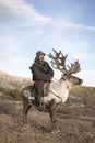 tsaatan man, dressed in a traditional deel, riding his reindeers