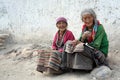 Two very old women in national costumes are sitting by the whitewashed wall in the street.