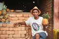 Tsiafahy, Madagascar - April 25, 2019: Local Malagasy man in straw hat and shirt selling pineapples at market, holding one fruit Royalty Free Stock Photo