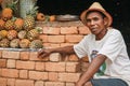 Tsiafahy, Madagascar - April 25, 2019: Local Malagasy man in straw hat and shirt selling pineapples at market, looking to camera,