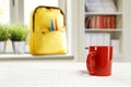 Ttable top with empty space for products or decoration, yellow schoolbag, red mug, blurred spring outside the window background. Royalty Free Stock Photo