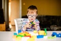 Little boy with syndrome dawn in the black glasses playing with blocks