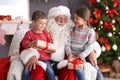 Little children with gift boxes sitting on Santa Claus` knees indoors Royalty Free Stock Photo
