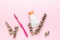 A tube of toothpaste, eucalyptus twigs and toothpaste on a pink background