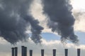 Tubes are releasing the dark smoke against a background of white clouds and a blue sky Royalty Free Stock Photo