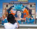 Female photographer photographs one of many distinctive murals in Tucson, Arizona, of an Hispanic woman on a warehouse