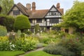 tudor house surrounded by lush gardens, with blooming flowers and shrubs