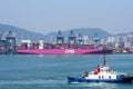 Tug boat sailing on the background of the large pink container ship