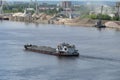The tug transports a barge loaded with sand along the river.