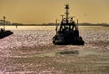 Tugboat leaves the harbor basin in the late afternoon and plunges into the open sea, backlight shot before sunset Royalty Free Stock Photo