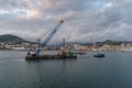 Tugboat pulls a crane-barge up beside the coastline