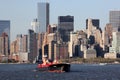 Tugboat pushing a barge RTC 82 across New York harbor, waterfront of the lower Manhattan in the background