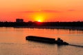 Tugboat pushing heavy long barge on the river Dnieper at sunset