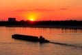 Tugboat pushing heavy long barge on the river Dnieper at sunset