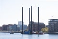 Tugboat towing a big barge through an urban harbor. The machine on the barge is for geotechnical studies. Modern residential build