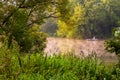 TULA, RUSSIA - AUGUST 12, 2013: A man fishing on river at inflatable boat at foggy summer morning under green foliage