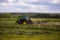 TULA, RUSSIA - JULY 30, 2019: green haymaking tractor on summer field before storm - telephoto shot with selective focus