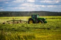 TULA, RUSSIA - JULY 30, 2019: green haymaking tractor on summer field before storm - telephoto shot with selective focus