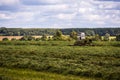 TULA, RUSSIA - JULY 30, 2019: green haymaking tractor on summer field before storm - telephoto shot with selective focus