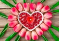 Tulip flowers are laid out in the shape of a heart on a wooden background, among them are a heart-shaped plate and a burning heart