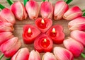 Tulip flowers are laid out in the shape of a heart on a wooden background, among them are lit candles in the shape of a heart. Royalty Free Stock Photo