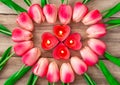 Tulip flowers are laid out in the shape of a heart on a wooden background, among them are lit candles in the shape of a heart. Royalty Free Stock Photo
