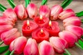 Tulip flowers are laid out in the shape of a heart on a wooden background, among them are lit candles in the shape of a heart.