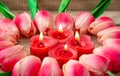 Tulip flowers are laid out in the shape of a heart on a wooden background, among them are lit candles in the shape of a heart.