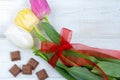 A tulips bouquet with red ribbon and pieces of chocolate on a white wooden background Royalty Free Stock Photo