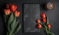 tulips and a candle on a black table with a slate board