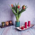 Tulips in a leafy vase and two candlesticks with candles.