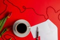 Tulips, white envelop with card, pen and cup of coffee on red background. Flat lay, top view.