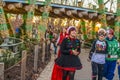 Girls in Christmas costumes walk under lighted rustic bridge with crowd and golden hour sun setting behind