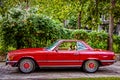 MERCEDES-BENZ 280SL PAGODA Burgundy red with black convertible with top up parked in driveway in leafy upscale neighborhood