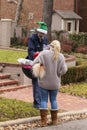 Postman wearing green Christmas elf hat pausing in his rounds to pet dog held by pretty blond neighborhood woman in sweater and Ug