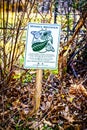 Sign for Monarch Butterfly Waystation posted near dormant brown shrubbery in early spring with just a few