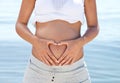 Tum time. a pregnant woman making a heart shape around her belly against a background of the ocean. Royalty Free Stock Photo