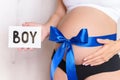 Tummy with blue ribbon and bow of pregnant caucasian woman which is holding nameplate boy