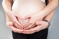 Tummy of pregnant woman with heart made of two pairs of hands.