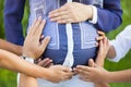 Tummy of pregnant woman wearing blue and white shirt with four pairs of hands