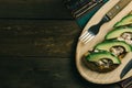 Tuna fish toast with mayonnaise and avocado served on a wooden plate with a fork on a coloured tablecloth on a wooden base
