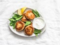 Tuna and potato patties served with spinach and greek yogurt on a light background, top view