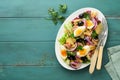 Tuna salad with pasta, eggs, potatoes, olives, red onions and sauce in white plate on old turquoise wooden rustic table background Royalty Free Stock Photo