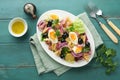 Tuna salad with pasta, eggs, potatoes, olives, red onions and sauce in white plate on old turquoise wooden rustic table background Royalty Free Stock Photo